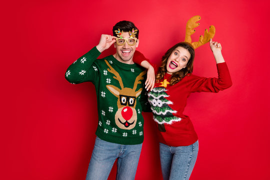 Portrait of funky crazy two people wife husband in brown antlers costume lean shoulder wear denim seasonal clothes christmas tree design pullover jumper spectacles isolated over red color background