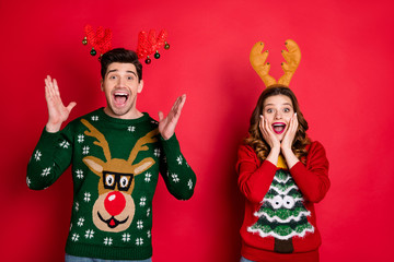 Portrait of amazed excited two people family wife husband brunet hair scream wow omg hear news wear season christmas tree hipster pattern pullover sweater isolated over red color background