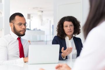 Business people interviewing job candidate. Business man and woman sitting at conference table with open laptop, and talking to employee sitting opposite. Employment meeting concept