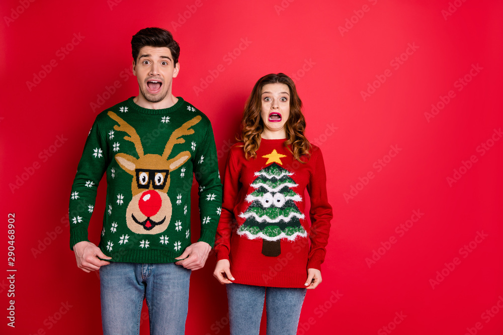 Poster Portrait of frustrated frightened two youth people with brunette wavy hair dislike christmas tree pattern decor jumper shout omg wear denim jeans isolated over red color background