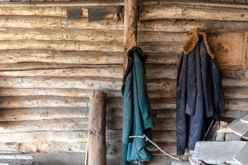 Two old coats hang on the wooden wall of a shed abandoned in the village by firewood and branches.