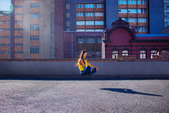 Beautiful woman in jeans and a yellow top levitating on a rooftop.