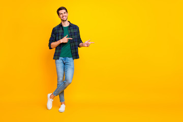 Fototapeta na wymiar Copyspace full length body size photo of cheerful handsome guy wearing denim jeans checkered shirt footwear asking you to glance at empty space isolated over vibrant color background