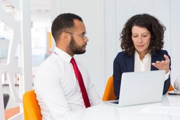 Project leader explaining job specific to newcomer. Business man and woman sitting at conference table with open laptop, talking and gesturing. Expertise concept