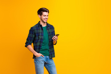 Fototapeta premium Photo of blogger guy holding telephone in hands checking subscribers wear casual checkered shirt and jeans isolated yellow color background