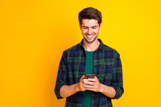 Photo of blogger guy holding telephone in hands checking subscribers wear casual checkered shirt isolated yellow color background