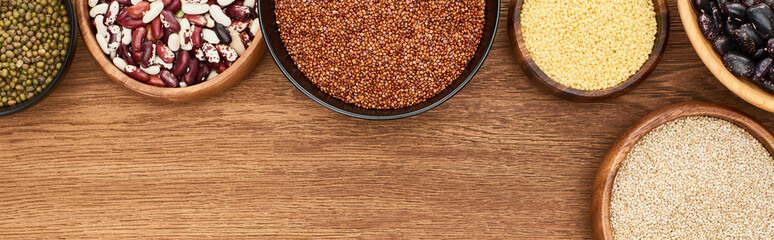 panoramic shot of bowls with buckwheat, couscous and beans on wooden surface