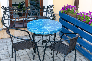 View of empty table in outdoor cafe on the street. coffee and restaurant terrace with metal elegant chairs, a blue table and floral design.