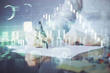 Hand taking notes in notepad. Forex chart holograms in front. Concept of research. Multi exposure