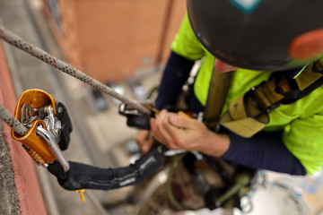 Fototapeta na wymiar Rope access inspector industrial abseiler wearing full body safety abseiling harness using self controller stop fall descent safety backup device energy absorbing lanyard attached while abseiling 