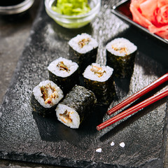 Macro shot of eel hosomaki sushi on natural black slate plate background with selective focus. Thin small unagi maki sushi rolls with rice, eel and nori closeup