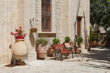 Fototapeta na wymiar Yard of old greek church in Cyprus. Limetone wall, flowers and sunny weather.