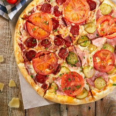 Pizza in half with salami, another - ham with pickled cucumbers and tomatoes sliced on wooden boards with vegetables