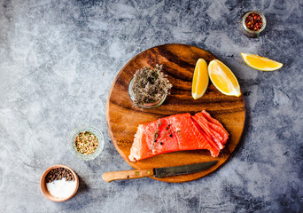 Slices of fresh raw salmon with peppercorns and rosemary on a gray background. Copy space. Top view.