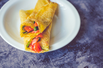 Thin pancakes with red fish on plate, top view.Crepes with filet salmon and cheese, red fish and green avocado on white plate over gray background.  Healthy breakfast