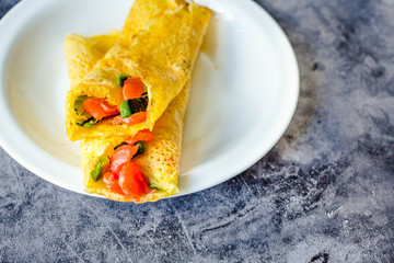 Thin pancakes with red fish on plate, top view.Crepes with filet salmon and cheese, red fish and green avocado on white plate over gray background.  Healthy breakfast