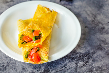 Thin pancakes with red fish on plate, top view.Crepes with filet salmon and cheese, red fish and green avocado on white plate over gray background.  Healthy breakfast