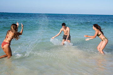 Two girls are splashing a boy in the waves