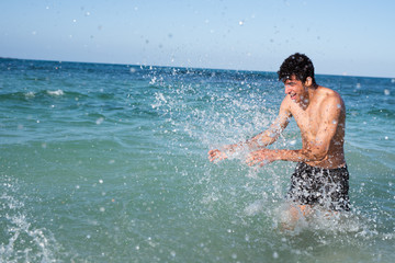 Young man being splashed by a wave in the ocean