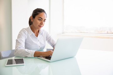 Focused female professional working on computer. Young Latin businesswoman sitting at workplace, using laptop, typing. looking at screen. Office worker concept