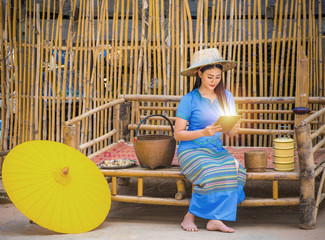 Asian women in blue local dresses using tablet or mobile device, Country life with yellow umbrella, tiffin carrier,Bamboo basket and Khene(Thai Musical Instruments), Technology in rural concept.