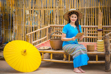 Asian women in blue local dresses using tablet or mobile device, Country life with yellow umbrella, tiffin carrier,Bamboo basket and Khene(Thai Musical Instruments), Technology in rural concept.