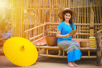 Asian women in blue local dresses using tablet or mobile device, Country life with yellow umbrella, tiffin carrier,Bamboo basket and Khene(Thai Musical Instruments), Technology in rural concept.