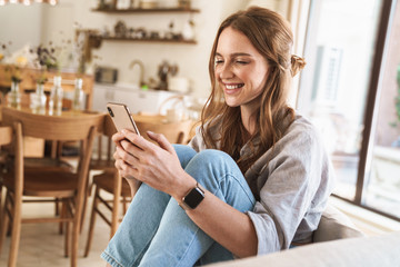 Smiling cheerful beautiful redhead woman at home using mobile phone.