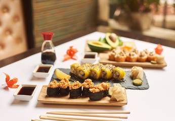 View of sushi roll topped with chopped seafood sticks. Table decorated with physalis, caviar and different vegetables. Delicious Japanese dish served with wasabi, soy sauce and marinated ginger.