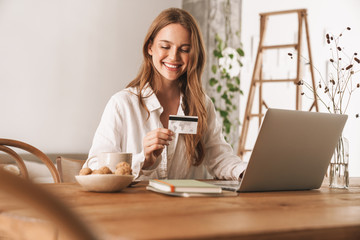 Woman sit indoors in office using laptop computer holding credit card.