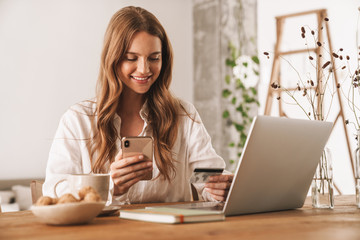 Woman using laptop computer and mobile phone holding credit card.