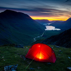 Wild camping tent illuminated with light at sunset in the Lake District looking down in the valley of Buttermere  © Mark
