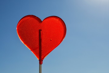 Red heart shaped lollipop against blue sky