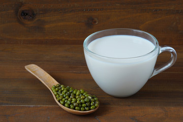 Glass with Soy Milk and Mung beans seeds in wood spoon on wooden background