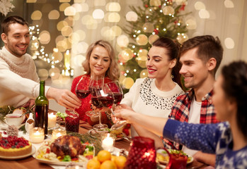 holidays and celebration concept - happy friends having christmas dinner at home, drinking red wine and clinking glasses