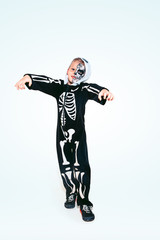 Little boy like a vampire in scary black costume with bones on white background. Caucasian male model looks scary. Halloween, black friday, sales, autumn holidays concept. The night of fear.