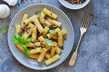 Rigatonni pasta with sauce and fried bacon on the kitchen table.
