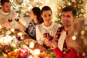 winter holidays and people concept - happy friends celebrating christmas at home feast and drinking red wine