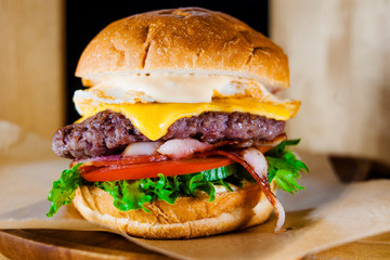 Large fresh burger with beef, vegetables, bacon, cream cheese, fried egg and sauce close-up.