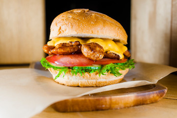 Burger with chicken, vegetables and cream cheese close-up on a wooden background in a restaurant.