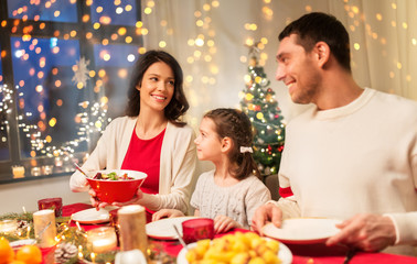 holidays, family and celebration concept - happy mother, father and little daughter having christmas dinner at home