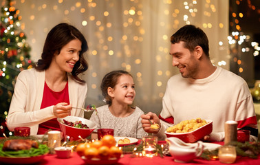 holidays, family and celebration concept - happy mother, father and little daughter having christmas dinner at home