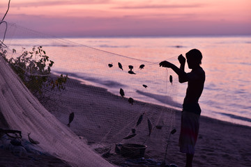 Silhouette of the indonesian fisherman removing fishes from the fishin net, Gİli Meno Island, Indonesia