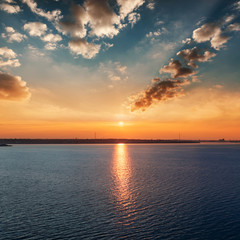 Naklejka premium red sunet over dark river. low dramatic clouds in red sun rays.