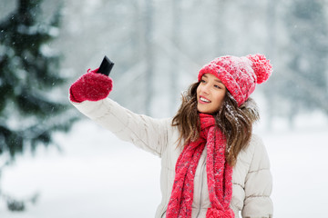 christmas, season and people concept - happy smiling teenage girl or young woman taking selfie by smartphone in winter park