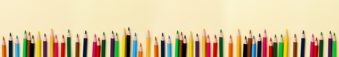 Multicolored wooden pencils for school on yellow paper background. School and office stationery on yellow background. Concept back to school. Banner with copy space.