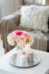 decoration, hygge and cosiness concept - candles burning on table and flowers at cozy home