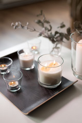 decoration, hygge and cosiness concept - burning white fragrance candles on tray on table at cozy home