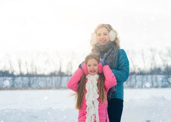Obraz premium Smiling young mother and her cute daughter ice skating together by hands. Family skating and training with white skates on the ice area in winter day. Weekends activities outdoor in cold weather.