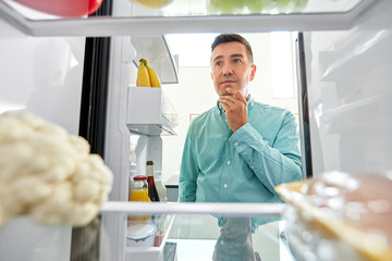 eating and diet concept - smiling middle-aged man man looking for food in fridge at kitchen
